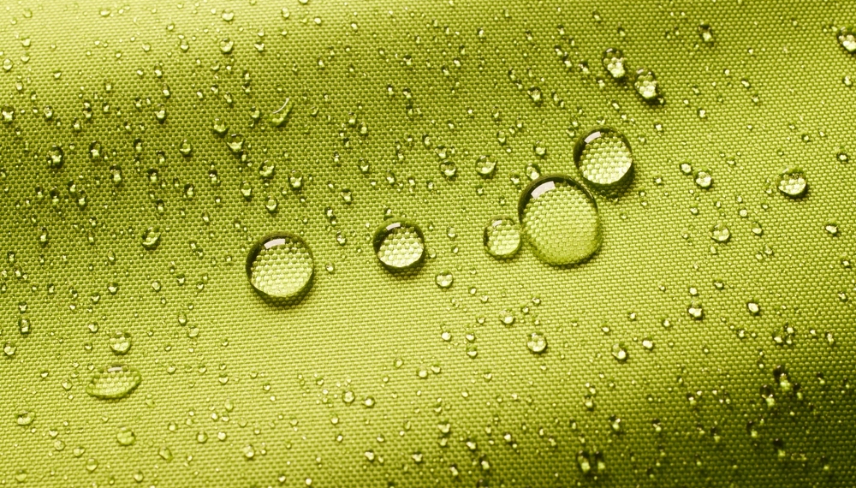 Top view closeup of green background with small round drops of water on textured waterproof impregnated fabric in light room