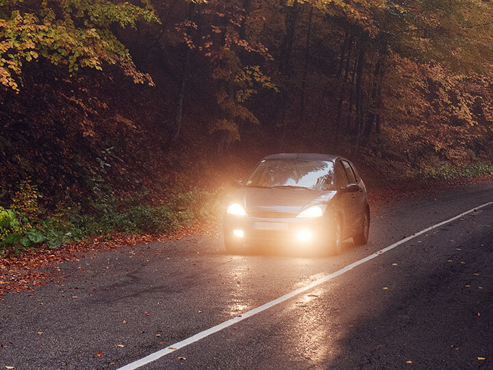 Car with headlights on driving down the road in a forest during autumn